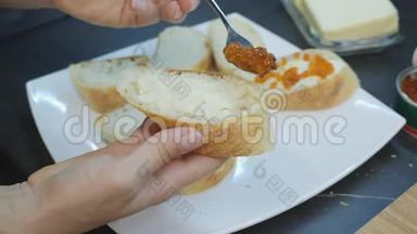 女人用勺子把红鱼子酱放在面包上。 夹上黄油和鱼子酱的三明治。 家庭烹饪。 女人播红鱼子酱